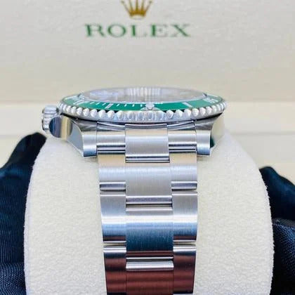 Rolex watch with silver band and green bezel on a white cushion, brand logo visible.